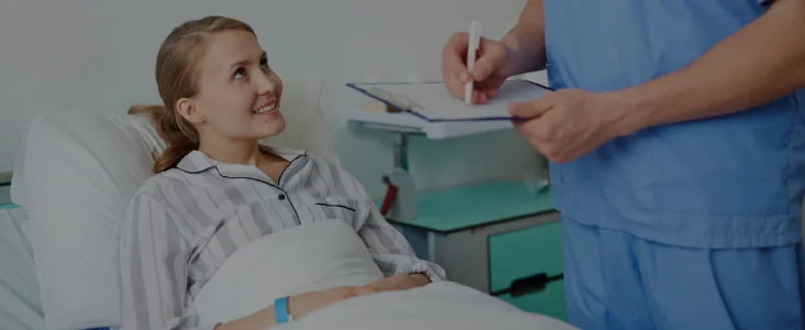 Une enfant dans un lit d’hôpital aux côtés d’un soignant tenant un dossier.