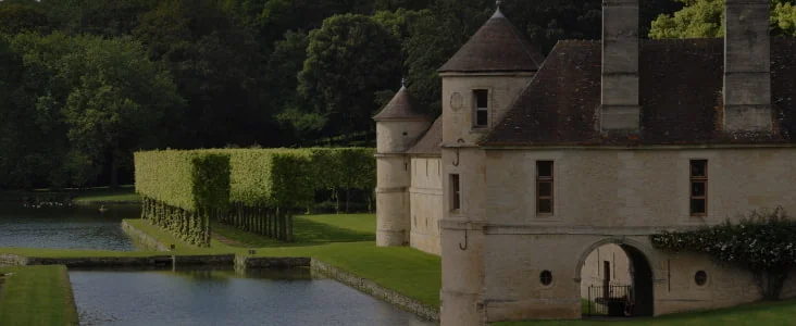 Château en pierre entouré d’eau et de jardins.