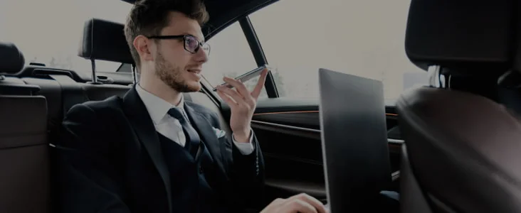 Un homme avec un ordinateur portable utilise son téléphone à l’arrière d’une voiture.