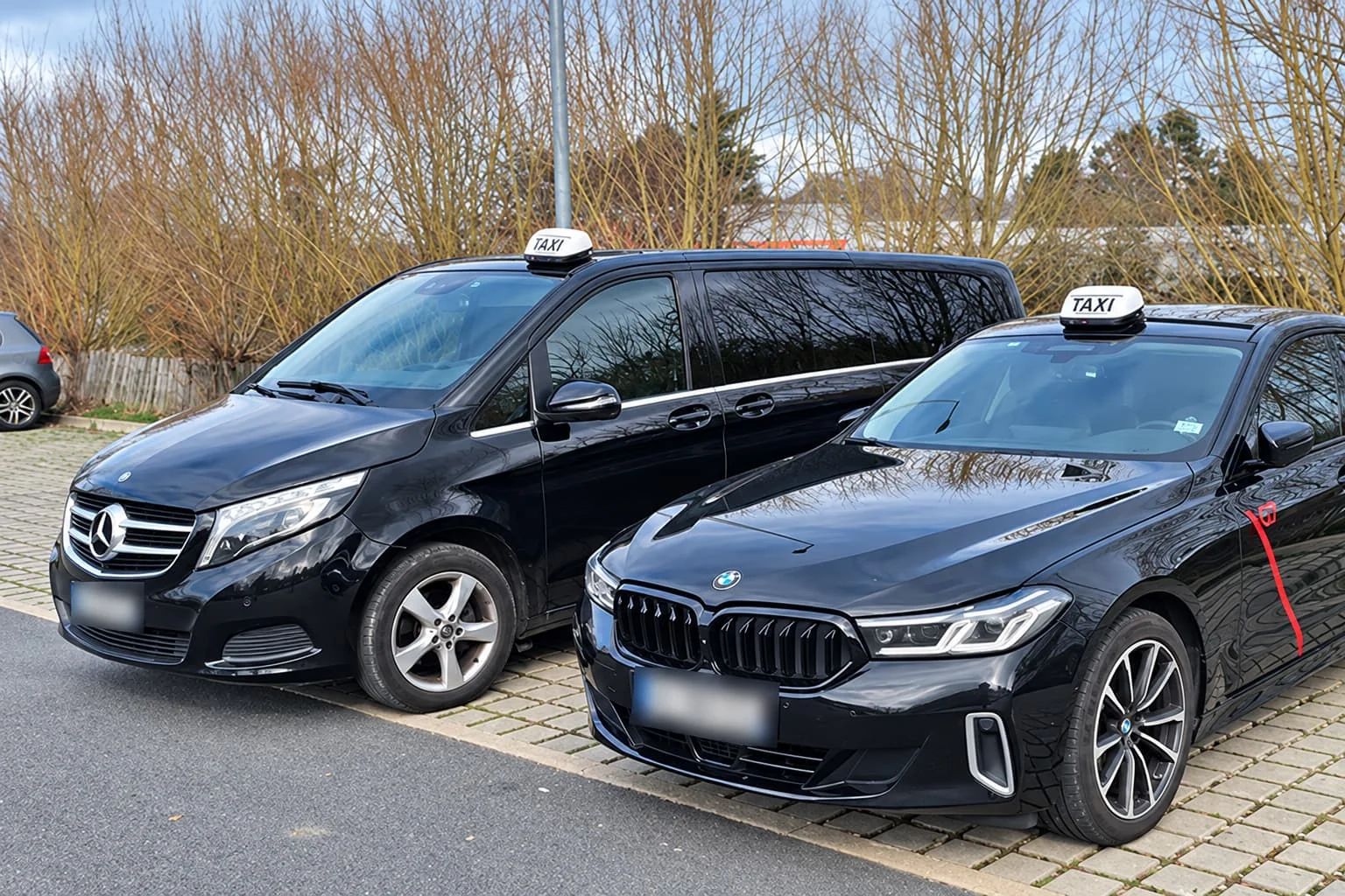 Un van Mercedes et une berline BMW équipés de lumineux taxi, stationnés côte à côte.